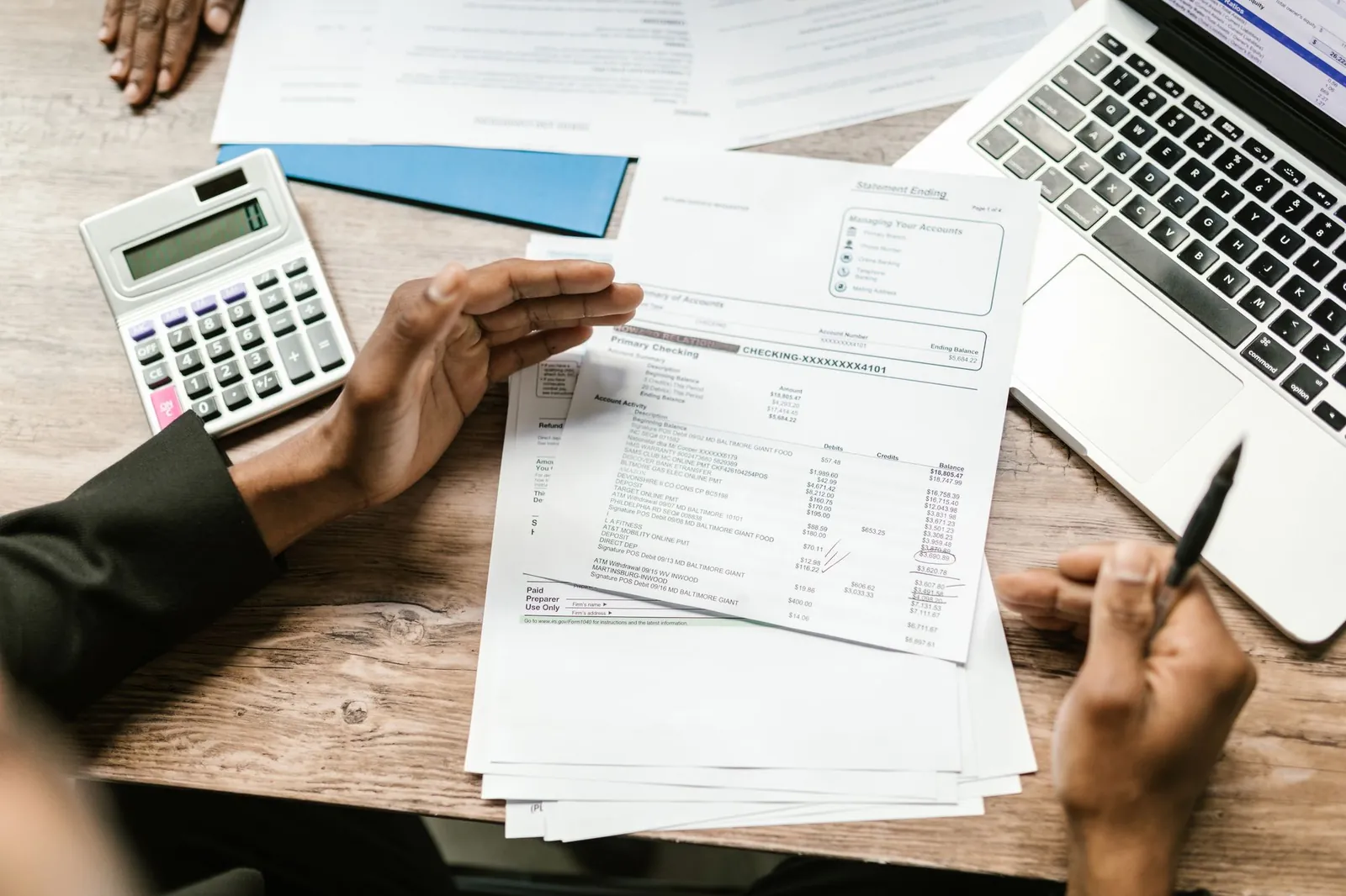 Handen met rekenmachine en financiële documenten op een bureau